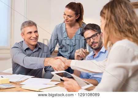 Handshake after a job recruitment meeting. Successful businesspeople shaking hands in front of their colleagues. Mature businessman shaking hands to seal a deal with businesswoman in office. 
