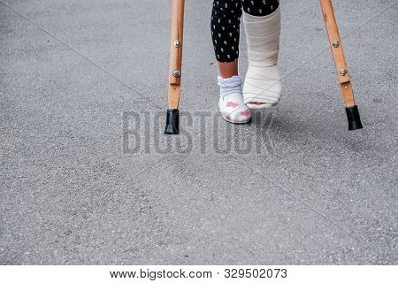 Kid With Broken Leg Is On Crutches On The Street. Conceptual Photo Depicting A Child With A Broken L