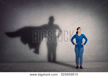 Brave Woman Keeps Arms On Hips, Smiling Confident, Casting A Superhero With Cape Shadow On The Wall.