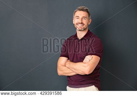 Portrait of smiling mature man standing on gray wall with folded arms. Successful mid adult man with folded arms standing over grey background while looking at camera with copy space.