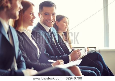 Row of business people making notes at seminar with focus on smiling young man