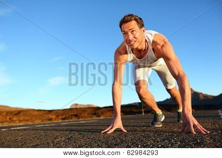 Sprinter starting sprint - man running getting ready to start sprinting run. Fit male runner athlete training outside on road in beautiful mountain landscape nature.