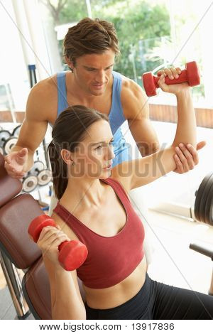 Young Woman Working With Weights In Gym With Personal Trainer