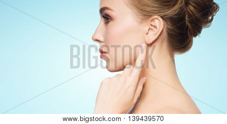 health, people and beauty concept - beautiful young woman pointing finger to her ear over blue background