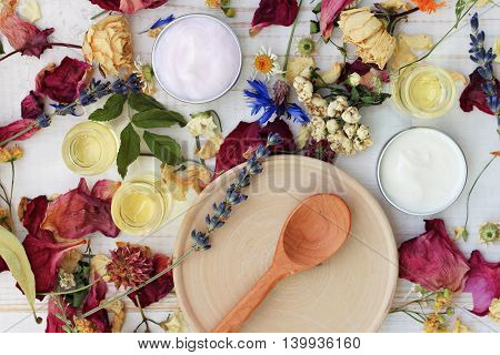 Dried herb mix, wooden plate spoon, moisturizer, lotion, essential oils. Herbal skincare spa preparation, top view.