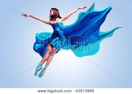 Beautiful ballet dancer with flowing blue fabric dancing with grace in studio