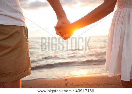 Zomer paar hand in hand bij zonsondergang op het strand. Romantische jong koppel genieten van zon, zon, romanc