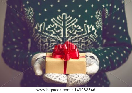 Girl holds in hands Christmas present. Christmas background. Gifts for men. Knitted mittens. Knitted dress. 2017 year. Box with gifts. Merry Christmas. Toned image.