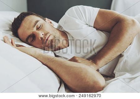 Handsome Man Sleeping In His Soft Bed At Some. Young Guy Wearing White Tshirt. People And Healthcare