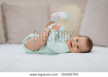 Playful baby lying down in bed. Happy baby lying on white sheet and holding her legs