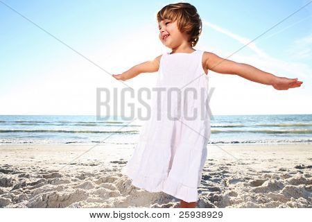 Small cute girl in white dress enjoying sunny day at the beach. Shoot against the sun.