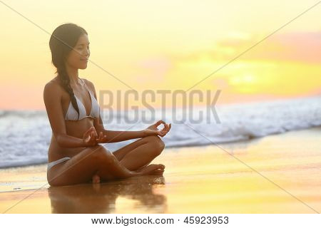 Meditação - Yoga mulher meditando por do sol de praia serena e relaxante. Menina relaxante em pose de lótus 