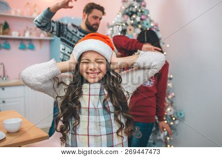 Small Girl In Festive Clothes Stands And Close Her Ears With Ahnds. She Has Closed Her Eyes. There A