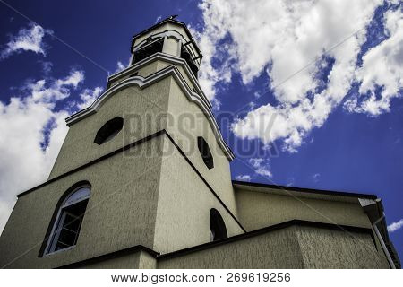 High Bell Tower Of The Temple Against The Cloudy Sky.