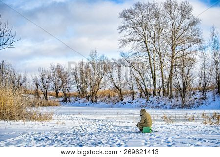 Fisherman Sitting On A Fishing Box On The Ice For Winter Fishing.