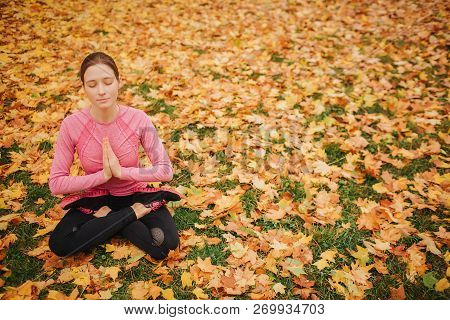 Calm And Peaceful Young Woman Sits In Lotus Position And Meditating. She Keeps Eyes Closed And Ahnds