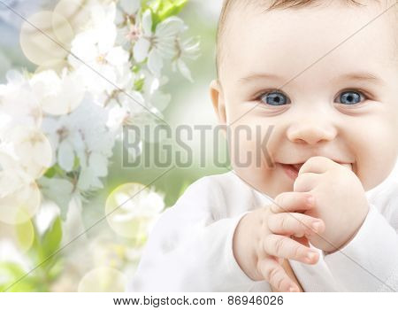 childhood, babyhood, summer, spring and health concept - closeup of happy baby boy or girl over green blooming garden background