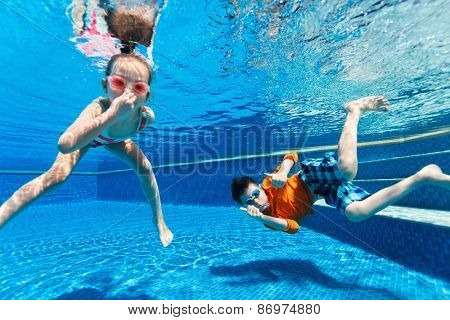 Kids having fun playing underwater in swimming pool on summer vacation