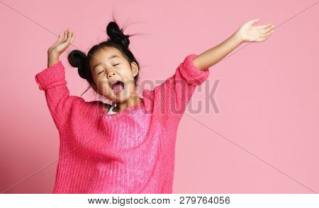 Asian Kid Girl In Pink Sweater, White Pants And Funny Buns Sings Singing Dancing On Pink Background