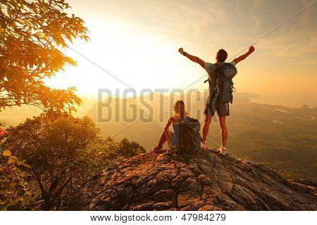 Two hikers enjoying sunrise from top of a mountain