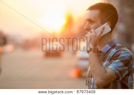 Young Man Making Call With Smartphone On Sunny Street