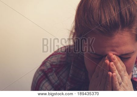 Crying unhappy woman covering her face with hands. Tired and depressed female on white background with copyspace. Emotional burnout, depression.