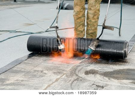 Roofing felt installation with heating and melting roll of bitumen roll by torch on flame