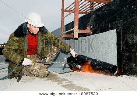 Roofing asphalt bitumen felt installation with heating and melting roll by torch on flame