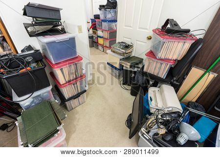 Messy office storage area with boxes, files, old equipment and miscellaneous clutter.  