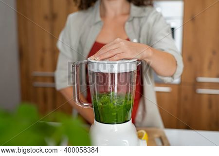 Close up of woman hands making healthy fruit smoothies in her kitchen. Fit girl making healthy detox drink using blender at home. Young woman making green vegan juice using machine.