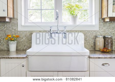 Kitchen interior with large rustic white porcelain sink and granite stone countertop under sunny window