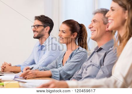 Happy business people in a row listening a seminar in office boardroom. A team of businesspeople sitting as panel for conducting job interview. Happy young team of business people a presentation.
