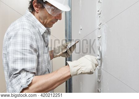 Man Drywall Worker Or Plasterer Putting Plaster On Plasterboard Wall Using A Trowel And A Spatula, F