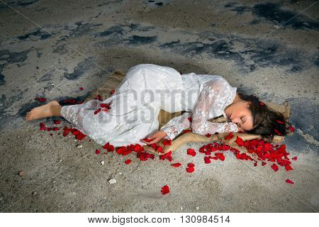 Young beautiful woman in antique lace gown sleeping in a derelict building with rose petals