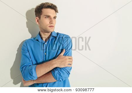 Side view of a young handsome man looking away from the camera while holding his hands crossed.