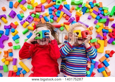 Happy preschool age children play with colorful plastic toy blocks. Creative kindergarten kids build a block tower. Educational toys for toddler or baby. Top view from above.