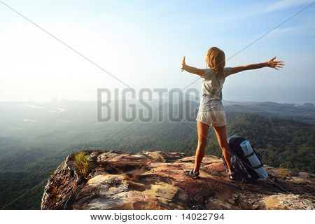 Jeune femme avec sac à dos, debout sur le bord de la falaise et à la recherche d'un ciel avec mains surélevées