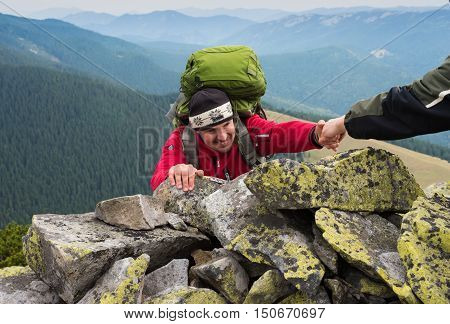 Helping hand - hiker man getting help on hike smiling happy overcoming obstacle. Hikers climbing on rock mountain at sunset one of them giving hand and helping to climb. Concept teamwork.