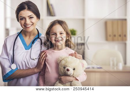 Friendly Doctor With Small Patient. Happy Girl And Doctor With Stethoscope. Joyful Nurse Plays With 