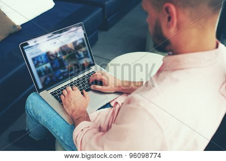 Back view young freelancer man busy working on laptop computer while sitting in modern coffee shop