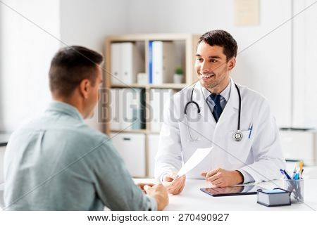 medicine, healthcare and people concept - happy smiling doctor giving prescription to patient at medical office in hospital