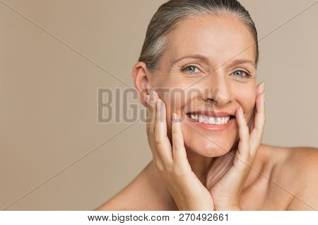 Beauty portrait of mature woman smiling with hand on face. Closeup face of happy senior woman feeling fresh after anti-aging treatment. Smiling beauty looking at camera with perfect skin.