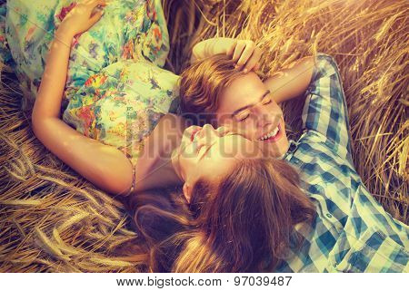 Beauty Couple Lying and relaxing on wheat field together. Teenage girlfriend and boyfriend having fun outdoors, kissing and hugging, first love concept. Teenagers Boy and Girl in love together