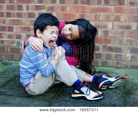 A young girl showing compassion to her little brother after he trips over and hurt his leg.