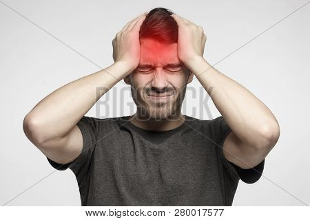 Young Man Isolated On Gray Background, Showing How Much Head Hurts, Experiencing Pain, Looking Miser