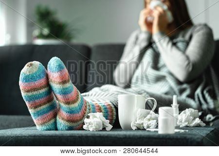 Sick Woman With Flu, Cold, Fever And Cough Sitting On Couch At Home. Ill Person Blowing Nose And Sne