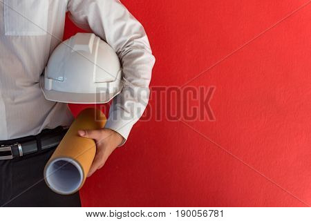 Engineer or Architect holding personal protective equipment safety helmet and architectural drawing in red background. Engineering Architecture and building construction management concepts