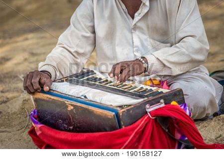 A old man is playing indian traditional musical instruments for kirtan harmonium.