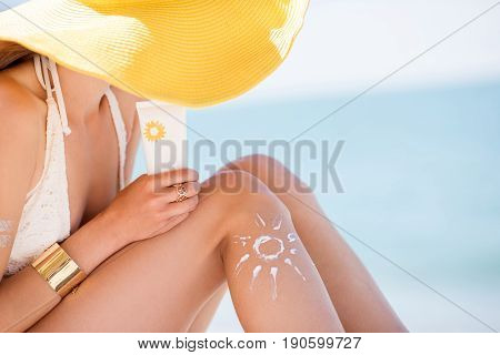 Beautiful woman in yellow hat sunbathing holding a bottle with sunscreen UV protective lotion on the beach