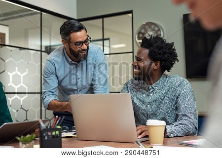 Two casual business partners sitting at table together and working. Group of smiling creative businesspeople working together. Mature businessman discussing affairs with african man in a meeting room.